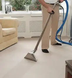 Professional carpet cleaner using a hot-water extraction wand and hose machine in a living room in Bakersfield, CA.