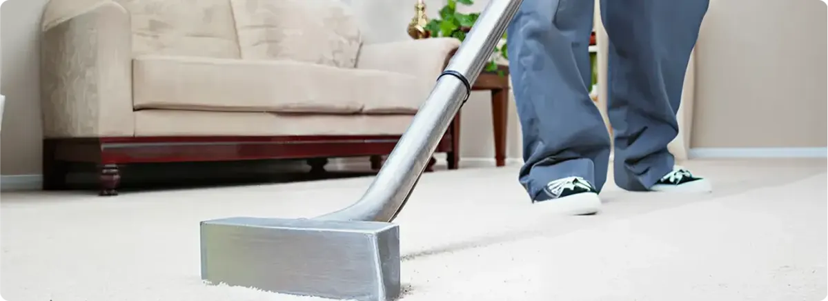 Carpet cleaning technician using a hot-water extraction wand on a light-colored carpet in a living room, Bakersfield, CA.