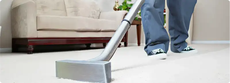 Carpet cleaning technician using a hot-water extraction wand on a light-colored carpet in a living room, Bakersfield, CA.