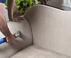 Professional upholstery cleaner deep-cleaning a fabric sofa with a handheld extraction tool and hose in Bakersfield, CA.